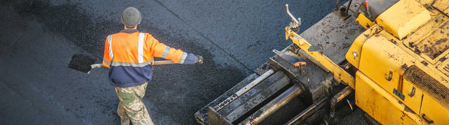 Worker shovels asphalt with heavy equipment